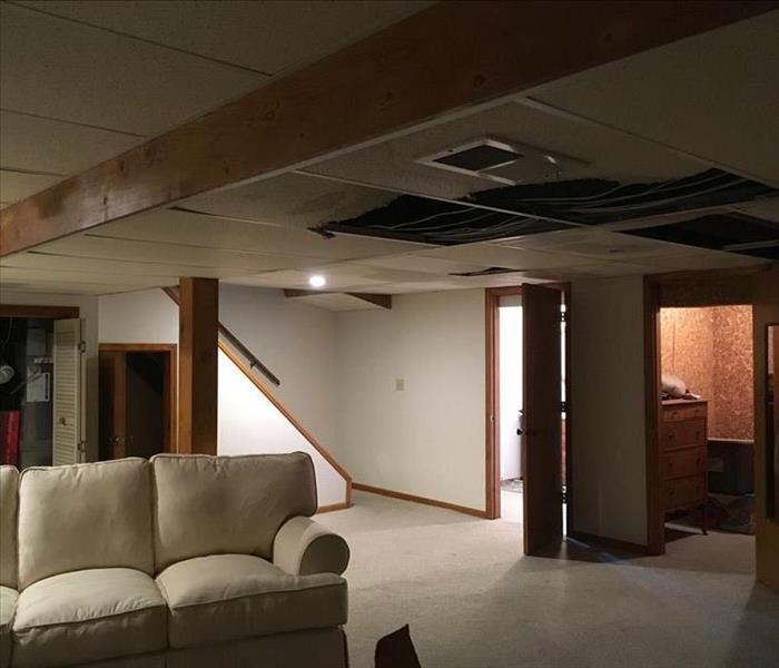 A carpeted basement room is shown with significant water damage to the ceiling tiles