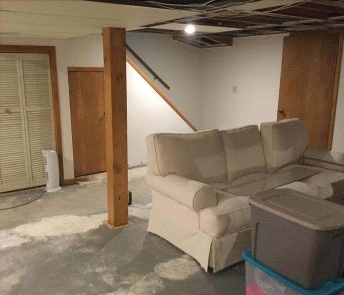 A basement room is shown after the cleanup is complete and the carpet as well as several ceiling tiles have been removed