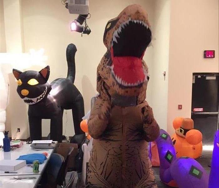 A SERVPRO employee in a blow up TRex costume with an inflatable Halloween cat behind him