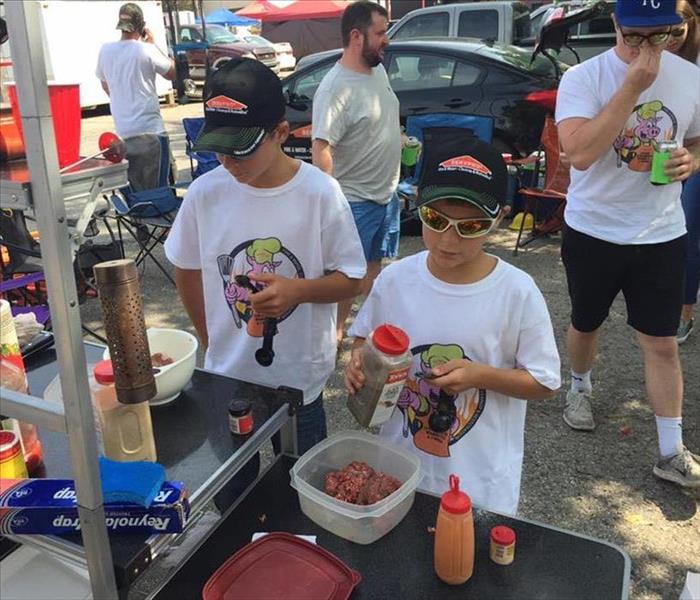 Two kids in SERVPRO hats are helping season meat for the Leavenworth BBQ Competition